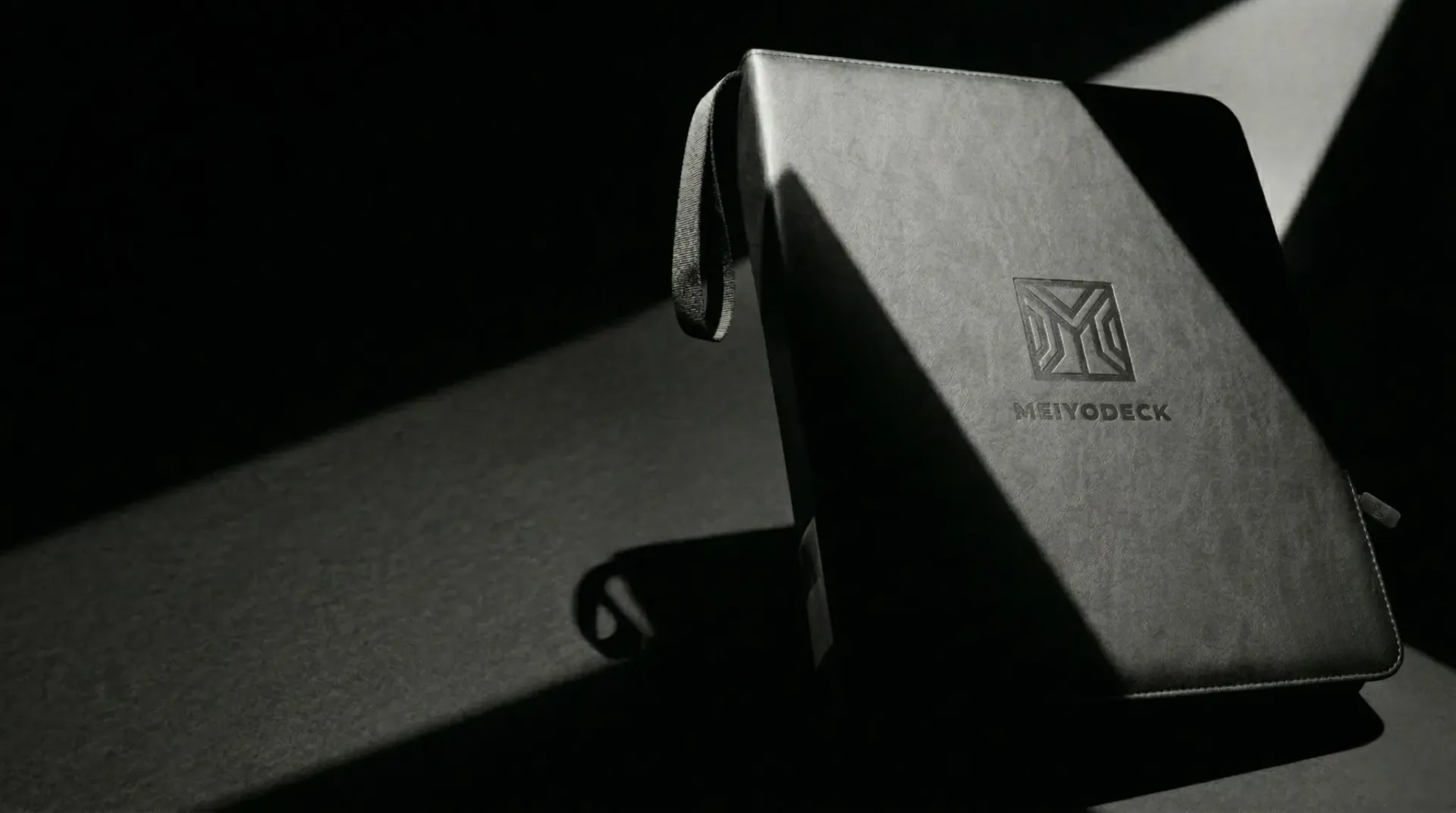 Meiyodeck top loader binder in black PU leather, lit against a dark editorial background